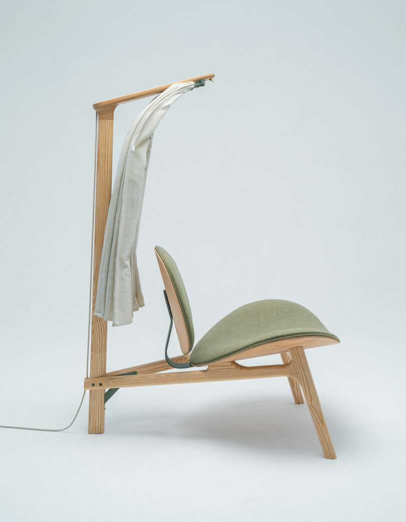 The Shanti Chair is a modern wooden lounge chair with green cushions, featuring a built-in light and a hanging white cloth, set against a plain background.