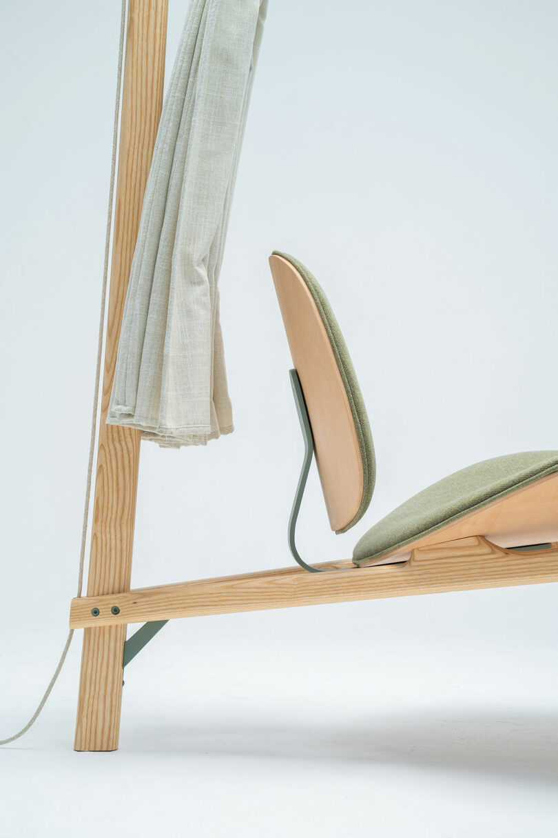 Close-up of the minimalist Shanti Chair with a green cushioned seat and backrest. A beige fabric hangs from the chair's frame.