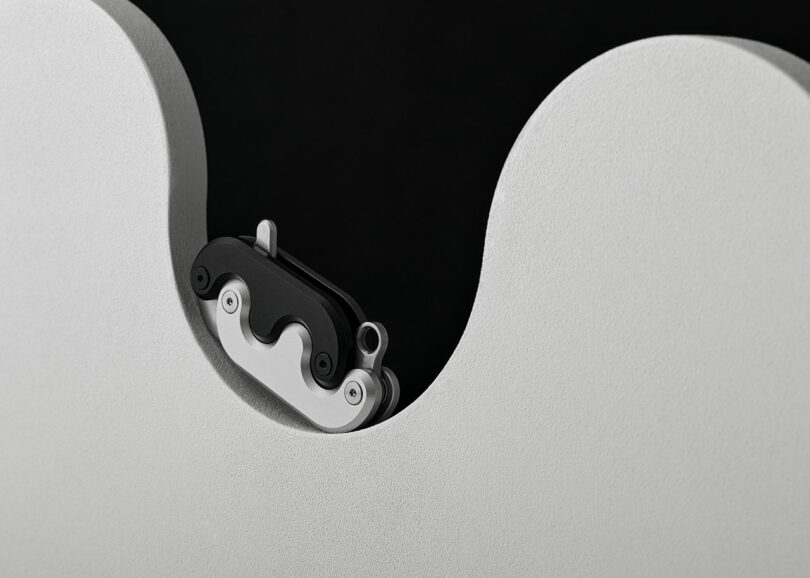 Close-up view of a silver and black mechanical component partially embedded in a smooth, curved, white surface against a black background.