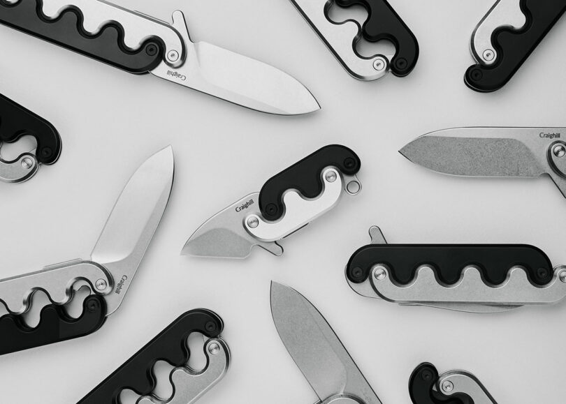 A collection of modern folding knives with silver blades and black handles arranged on a white background.