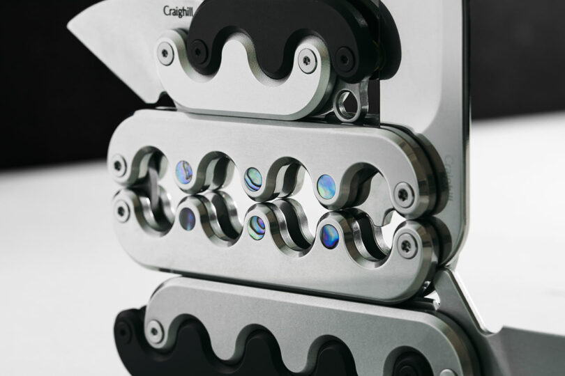 Close-up view of a detailed metal mechanism with interconnected curved components and multi-color reflective elements.