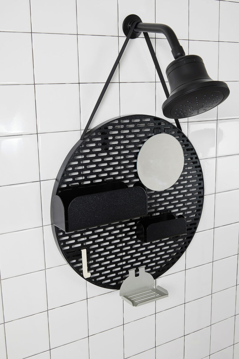 A circular metal organizer is hanging from a showerhead against a white tiled wall, featuring various compartments and shelves for bathroom essentials.