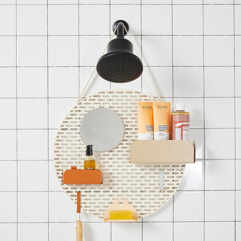 Shower caddy hanging under a showerhead on a tiled wall, holding various toiletries including bottles, soap, and a small mirror.