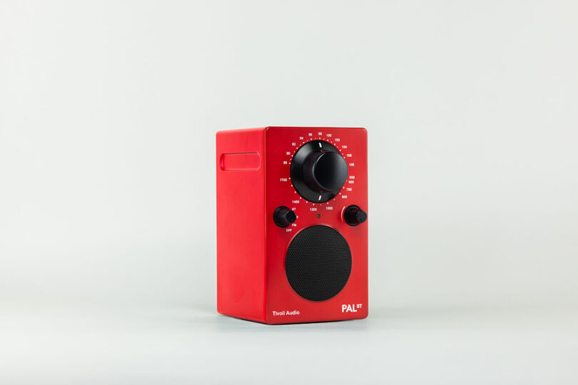 Red tabletop radio with Tivoli Audio's branding, featuring black knobs and a speaker grille. It has an analog tuning dial at the top and a volume control knob below. The model "PAL BT" is prominently displayed on the front, exuding classic charm.