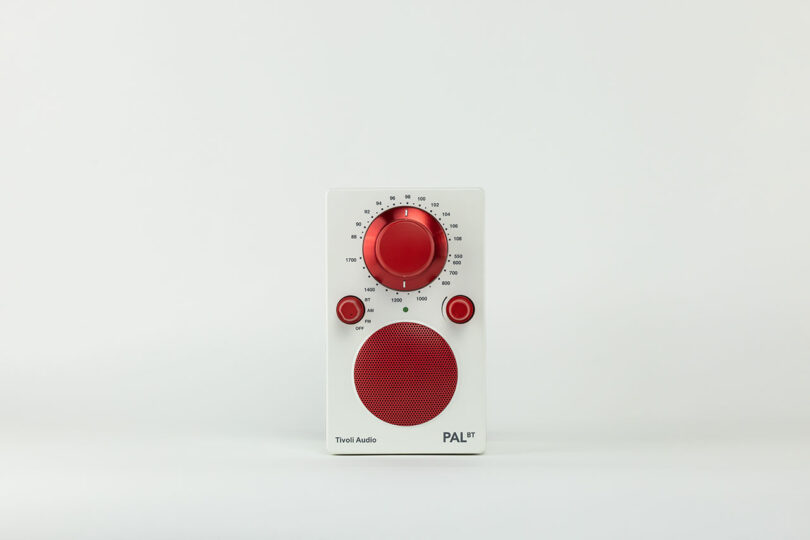 A small white and red Tivoli Audio portable radio with a large red dial, two smaller red dials, and a red speaker grille on a plain background.