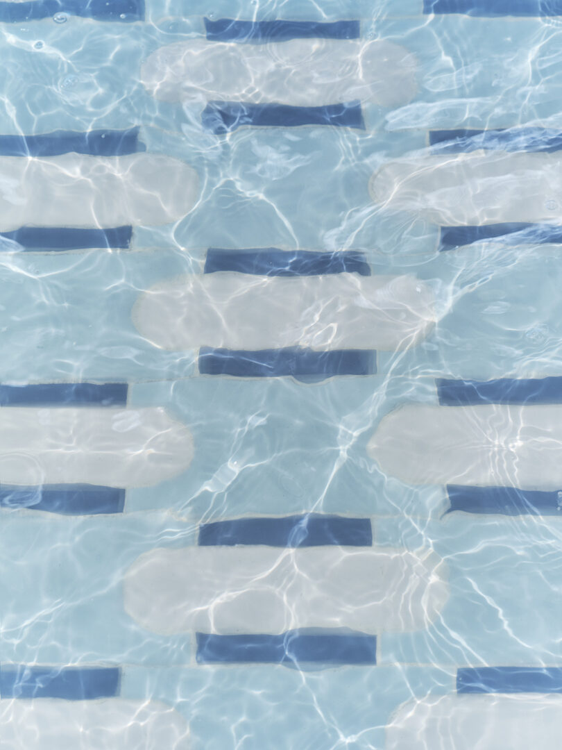 Underwater view of a swimming pool, showing Tivoli Tech light blue tiles with alternating dark blue and white rectangular patterns.