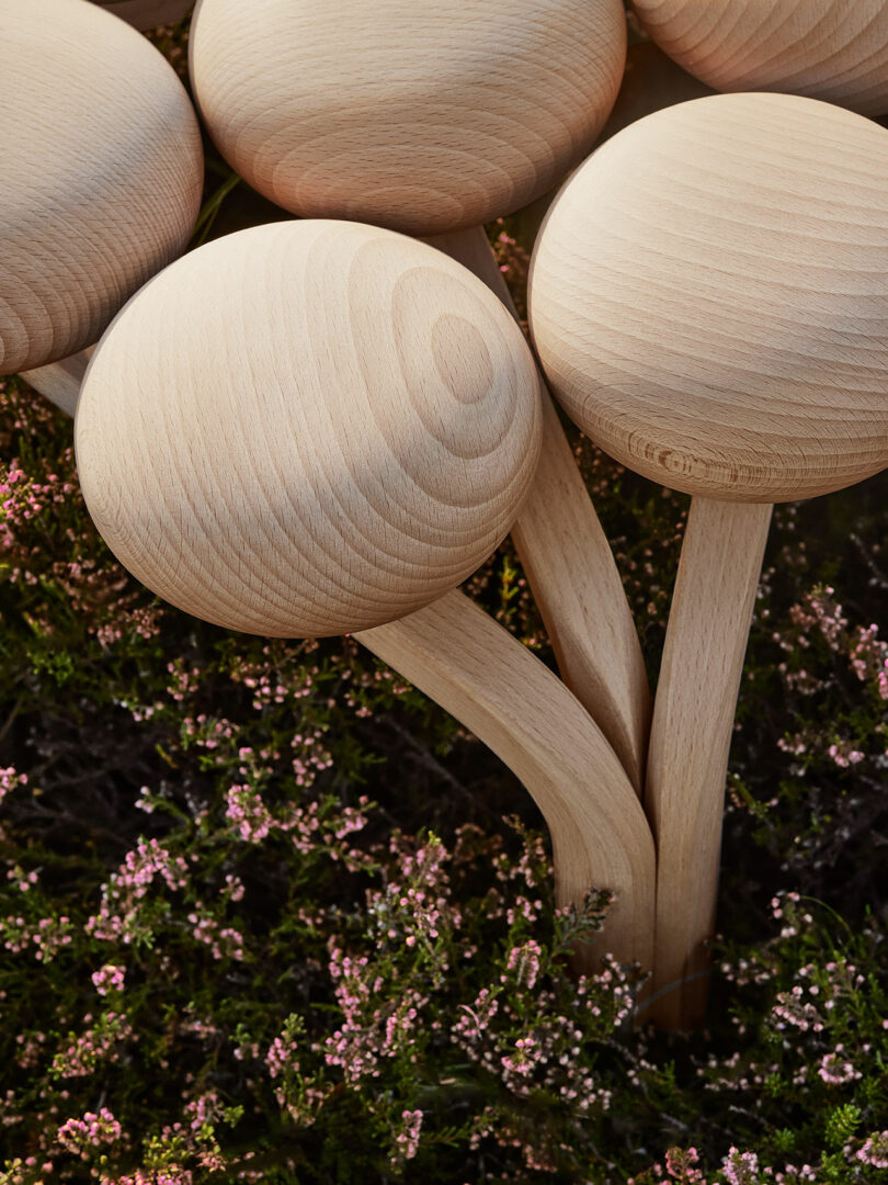 The top of the Utzon Stool, featuring protrusions resembling large mushrooms, with smooth, rounded caps and curved stems, positioned among small pink flowering plants.