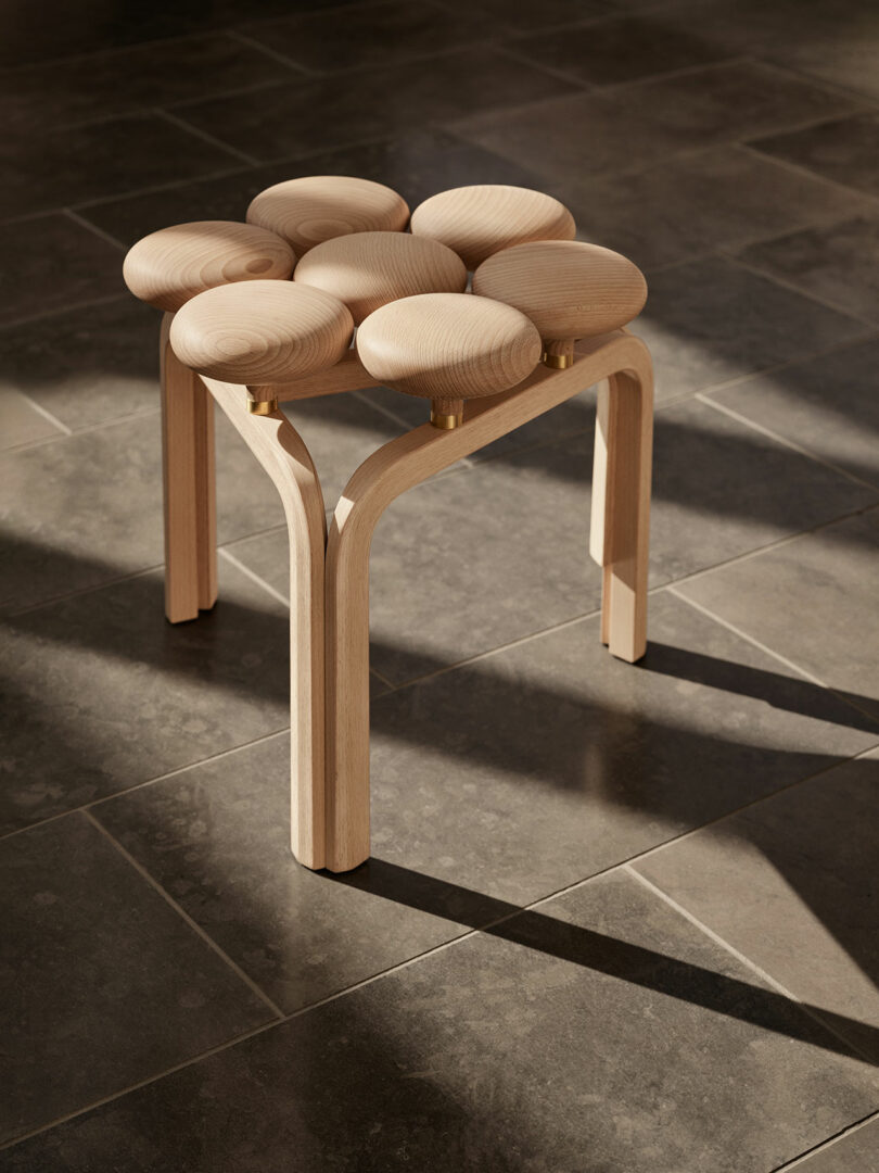 An Utzon Stool with a unique design featuring six rounded, cushion-like segments on top, standing on a tiled floor.