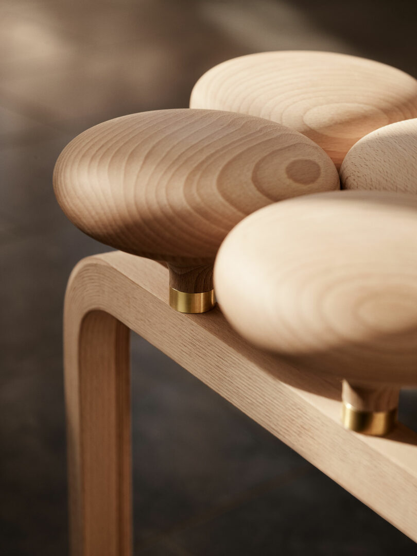 A close-up of an Utzon Stool with rounded, smooth-edged seats made of light-colored wood and brass fittings.