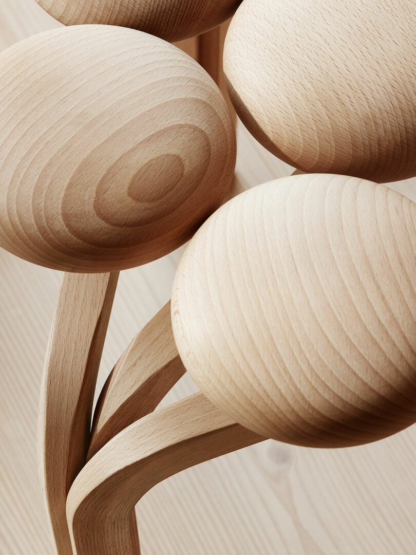 Close-up of the Utzon Stool featuring several sculpted, smooth wooden discs with natural grain patterns, interconnected by curved wooden stems.