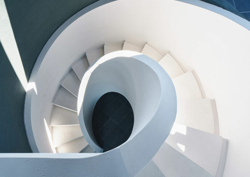 Top-down view of a white spiral staircase with sunlight casting shadows on the steps.