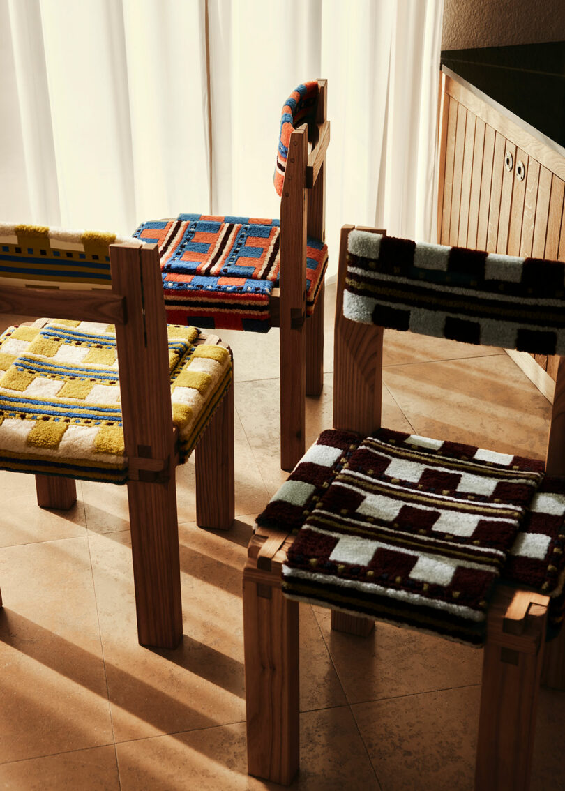 Four wooden chairs by Yves Salomon with brightly patterned fabric seats and backs arranged in a sunlit room with light-colored curtains and tiled floor.