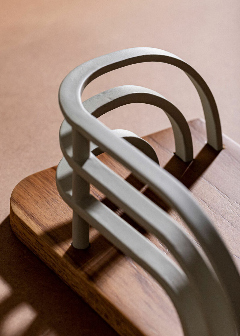 Curved metal bars attached to a wooden base, casting shadows on a surface