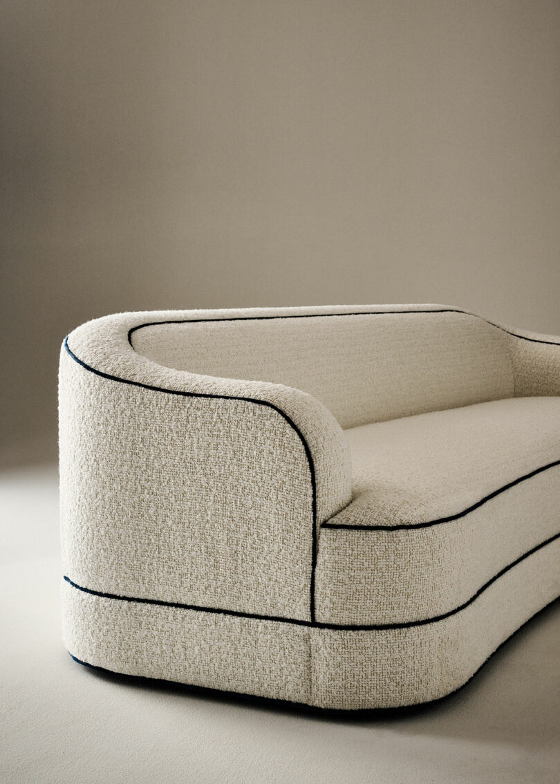 A beige, upholstered sofa with rounded edges and dark edging sits against a light background in neutral tones