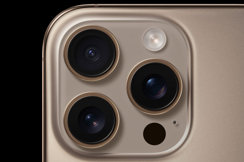 Close-up of the rear camera system on a gold-colored smartphone, showing three lenses and a flash.