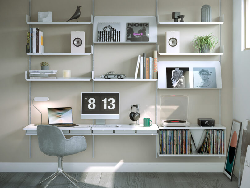 Modern home office setup with a desk, chair, computer, turntable, plants, vinyl records, books, and decor items on wall-mounted shelves. Natural light coming from the right.