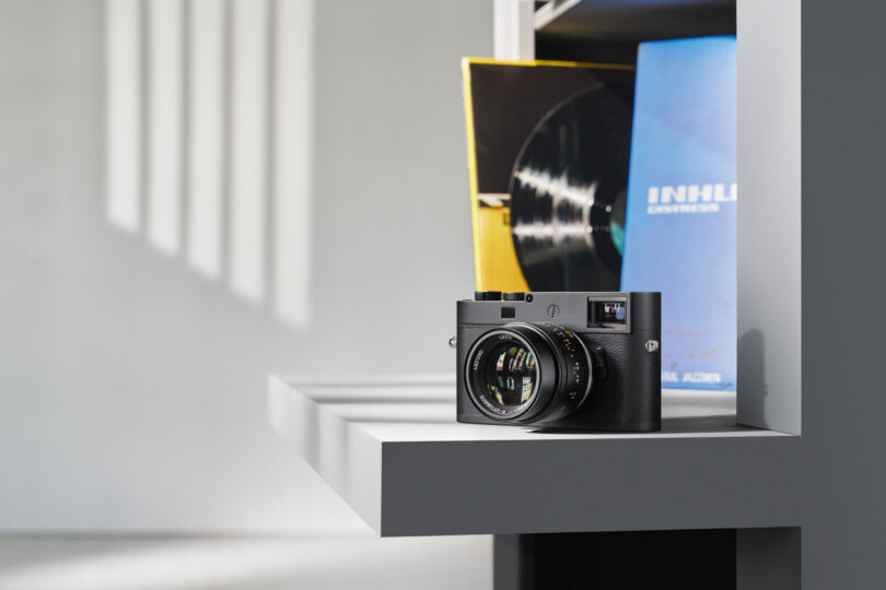 A black camera sits on a white shelf, with LP album covers partially visible in the background.