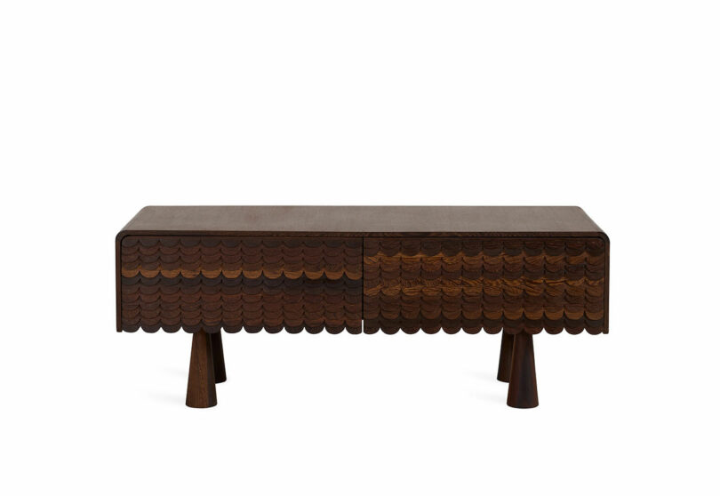 A dark wooden console table with a scalloped design on the front and four tapered legs