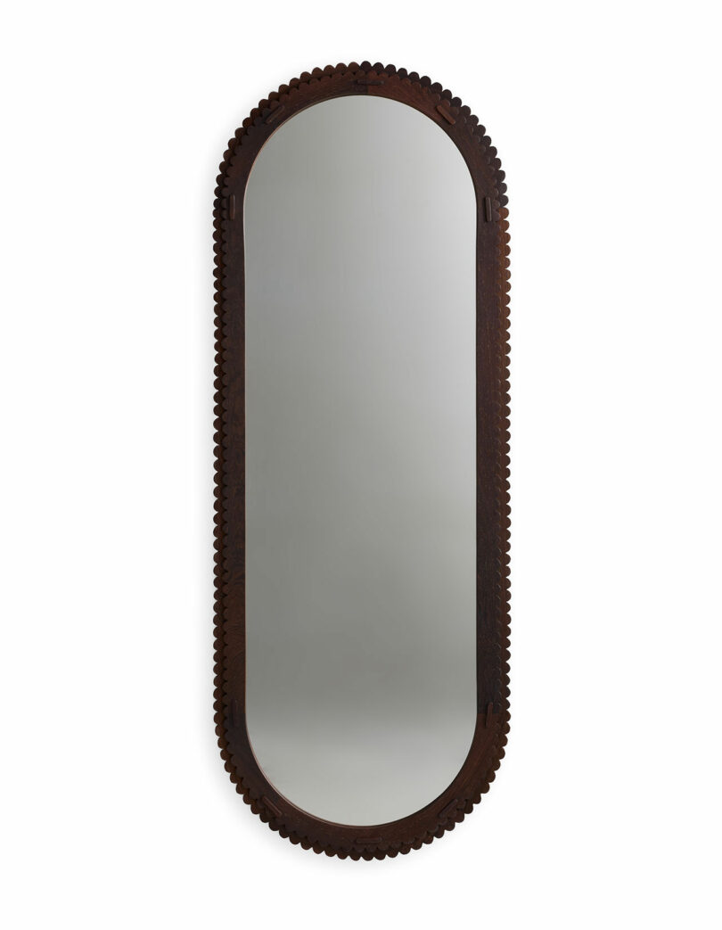 An oval wall mirror with a dark, intricately carved wooden frame