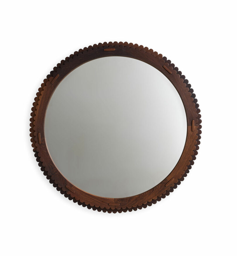 A round mirror with a decorative dark wooden frame featuring scalloped edges