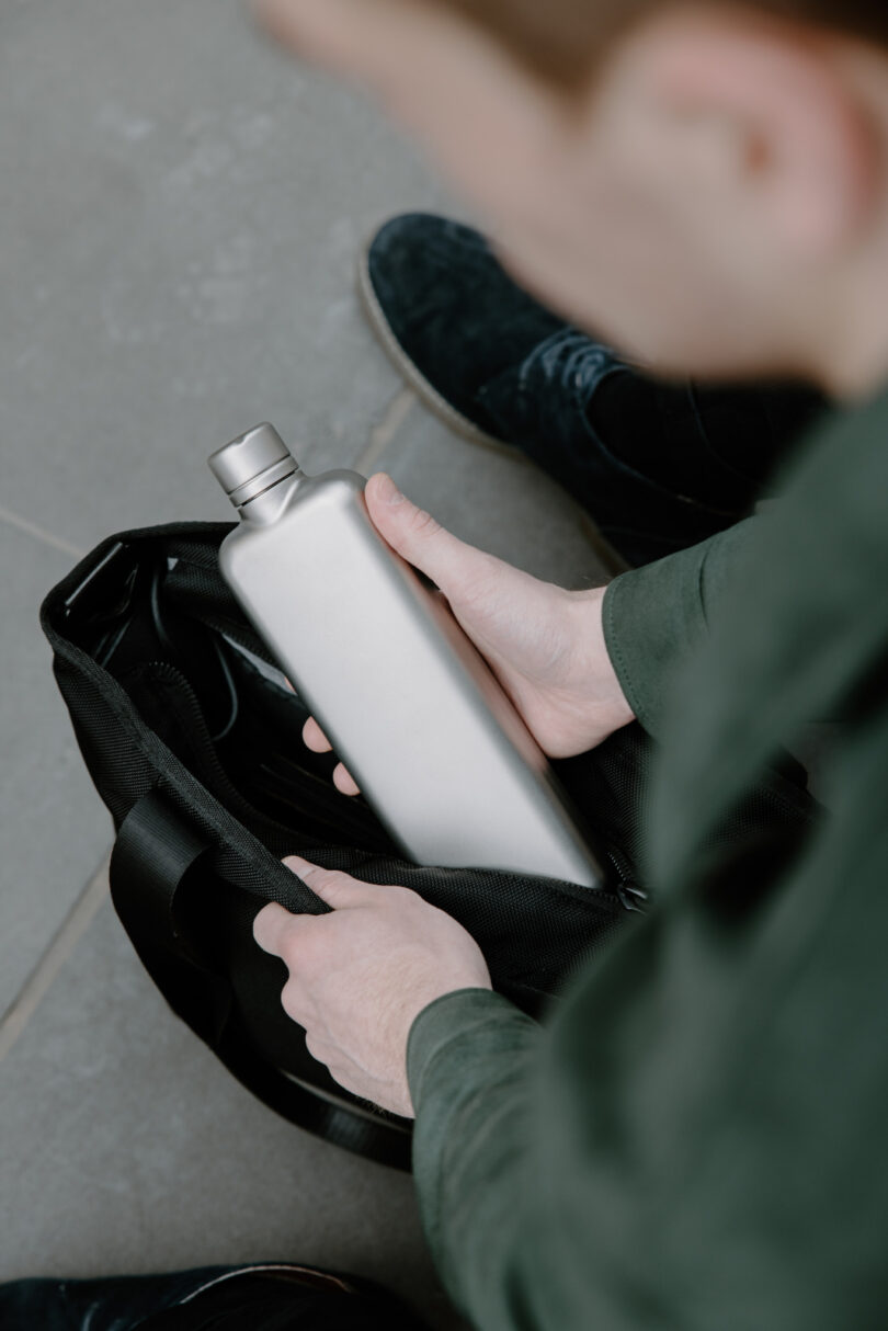 Person placing a silver metal water bottle into a black bag