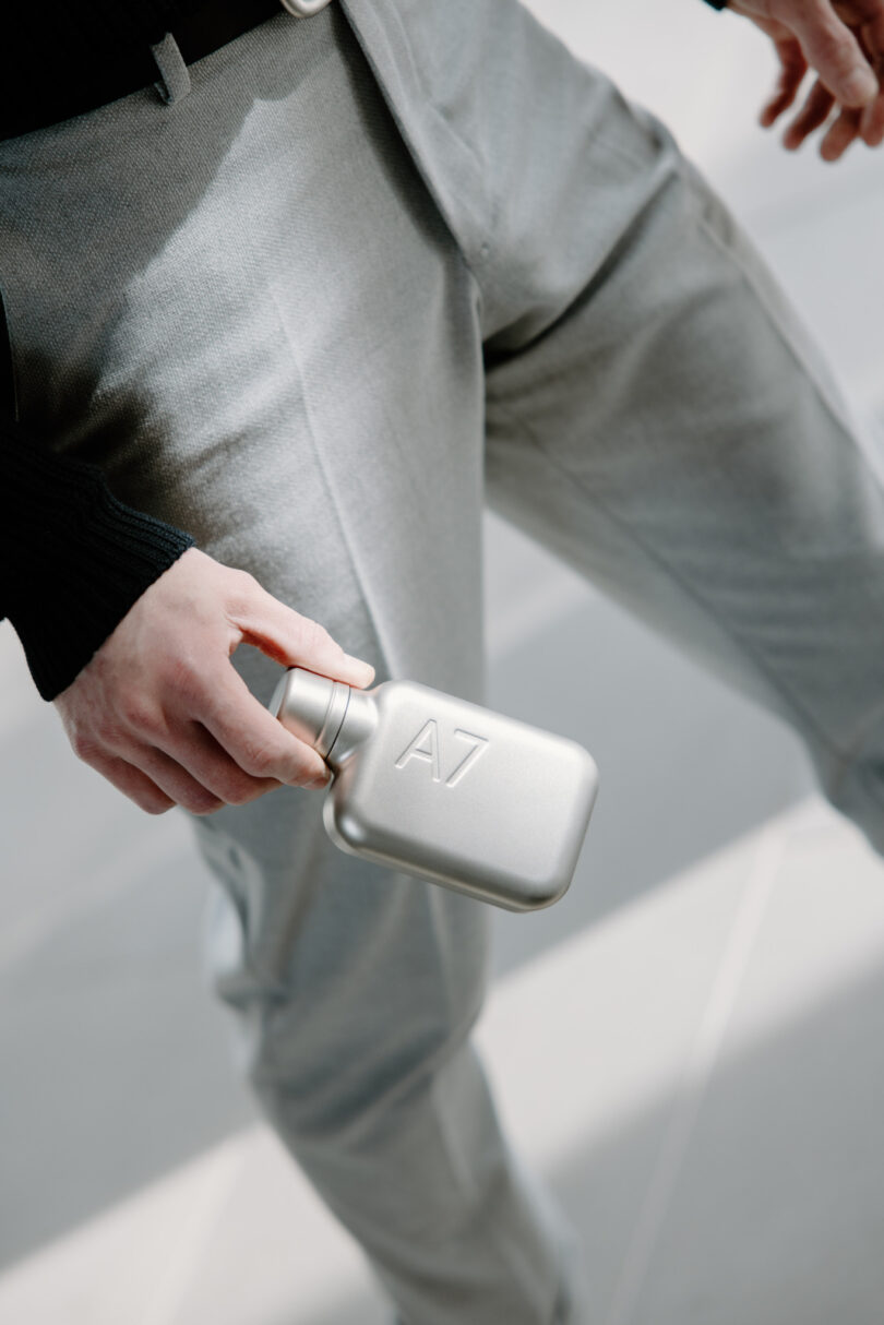 A person in gray pants holding a small silver rectangular bottle labeled "A7"