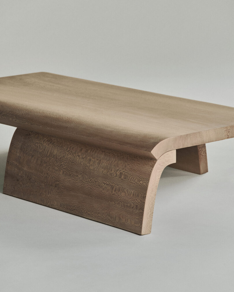 A sleek, minimalist wooden coffee table with curved legs on a plain background.