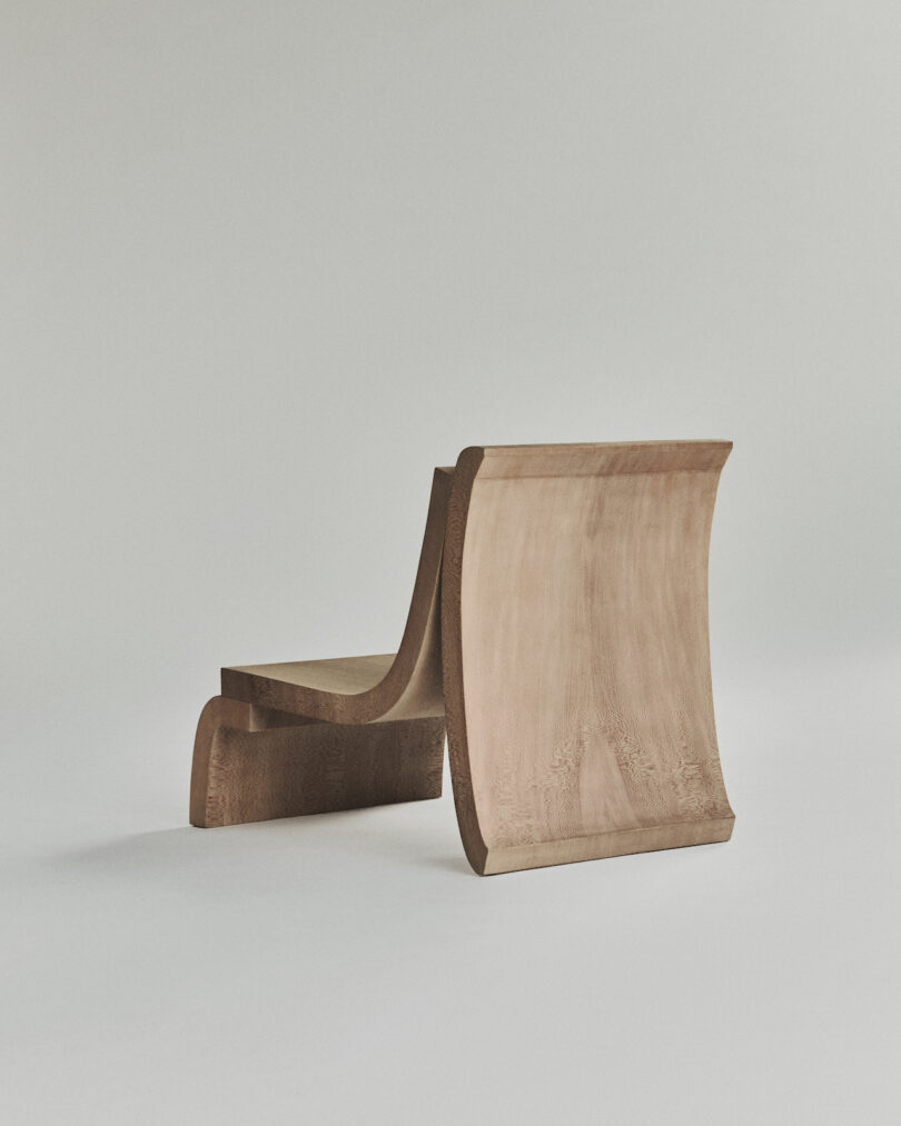 A minimalist wooden chair with an unconventional, curving design on a plain background.