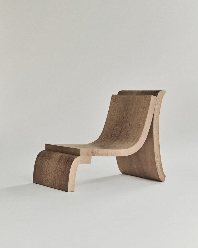 A wooden chair with a flowing, curved design and a minimalist aesthetic on a plain background.