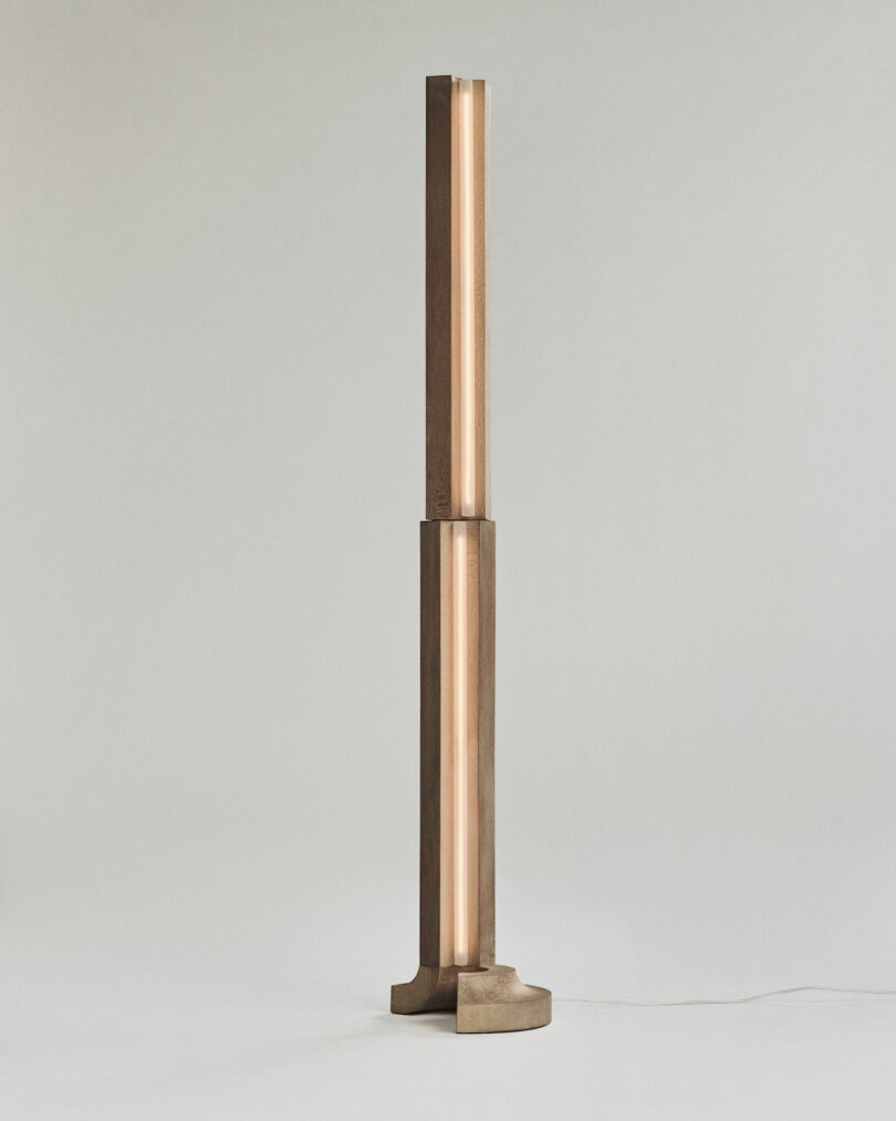 A tall, modern floor lamp with a cylindrical design, featuring a vertical light strip in the center and a sturdy base, set against a plain background.