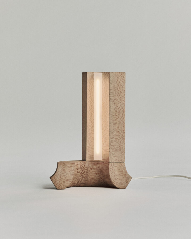 A wooden table lamp with a vertical light strip in the center is lit, set against a plain background.