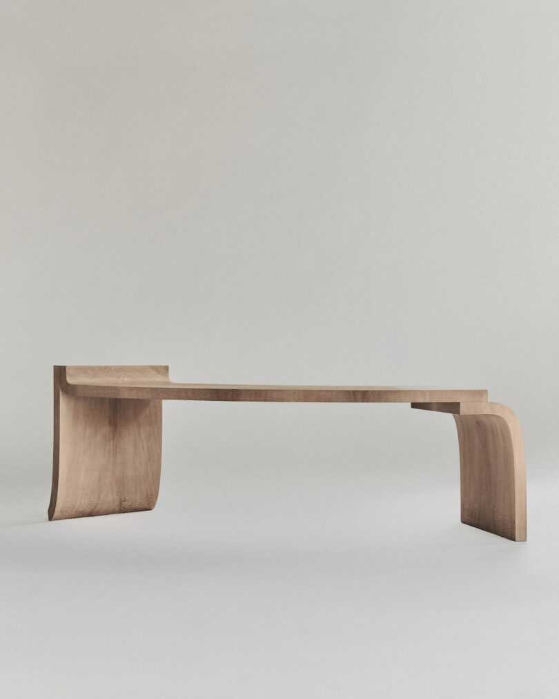 A minimalist wooden bench with a flat seat and curved legs set against a plain background.