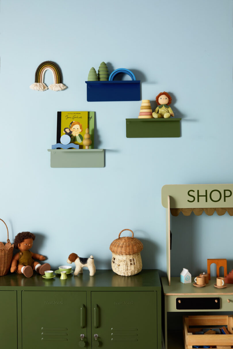 Children's play area with toys, books, and decorative items on shelves and a play kitchen setup labeled "SHOP" against a light blue wall