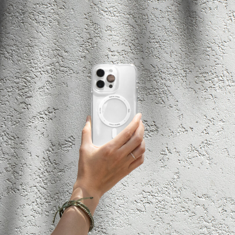 A hand holding a smartphone with a circular mount on its back, positioned against a textured gray wall.