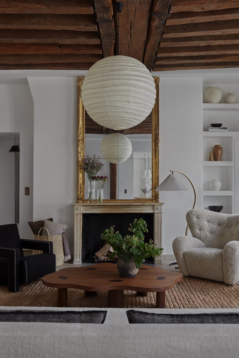 A view of the living room, with exposed wooden beams, a stone fireplace, and carefully curated pieces