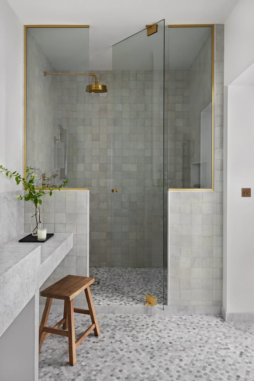 A detail shot of a sleek, contemporary bathroom with brass fixtures and soft grey tiles