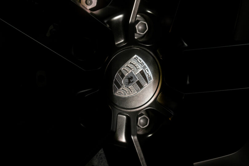 Close-up of a car's black alloy wheel, showing the central hub with the Porsche logo prominently displayed.