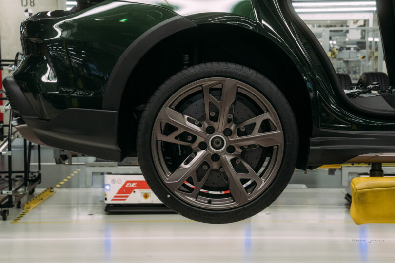 Close-up of a mounted car wheel with a detailed alloy rim and brake system in a brightly lit automotive factory.