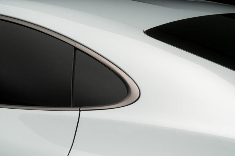 Close-up of a car's sleek, white body with tinted windows, showing the rear door and window seamlessly integrated with a smooth, aerodynamic design.