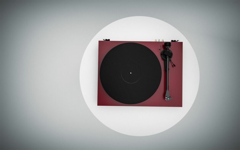 Top view of a Pro-Ject Debut EVO 2 turntable in red and black with a minimalist design on a light gray background.