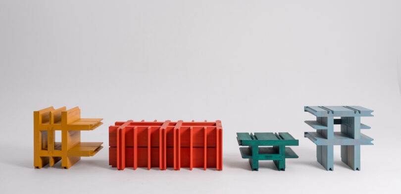 Four colorful, abstract sculptures of varying sizes are arranged in a row against a plain white background. The sculptures are yellow, red, green, and blue from left to right