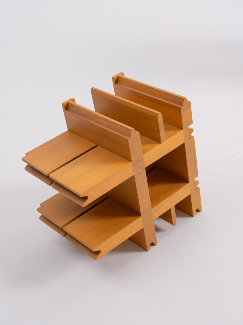 A small, wooden, modular shelving unit with multiple compartments on a light grey background