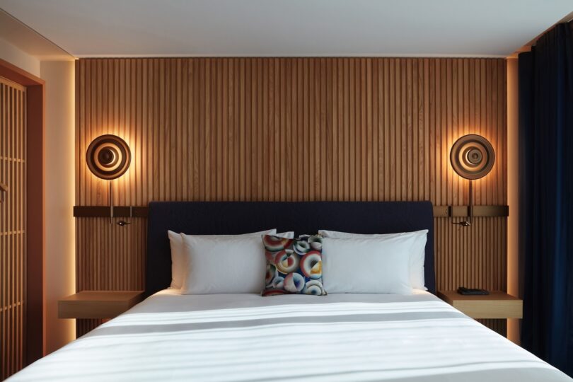 A close-up of a bed at SO/Paris, highlighting the wooden slat wall, warm lighting