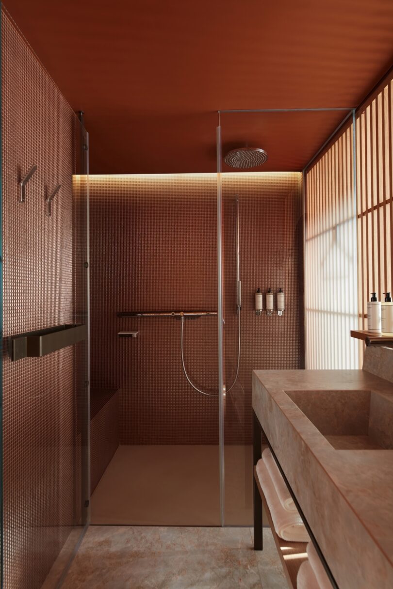 A sleek, minimalistic bathroom at SO/Paris with warm copper tones, a glass-enclosed shower