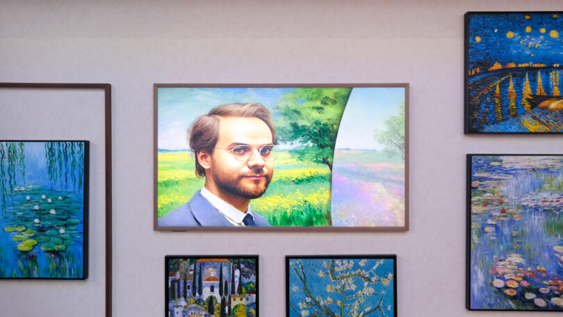 Portrait of a man wearing glasses in a suit displayed on a wall, surrounded by various colorful paintings depicting nature scenes.