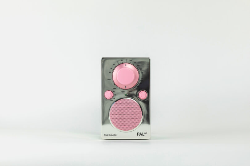 A retro-style portable radio with a silver and pink design, featuring a large speaker, volume knob, and tuning dial on a minimalistic white background.