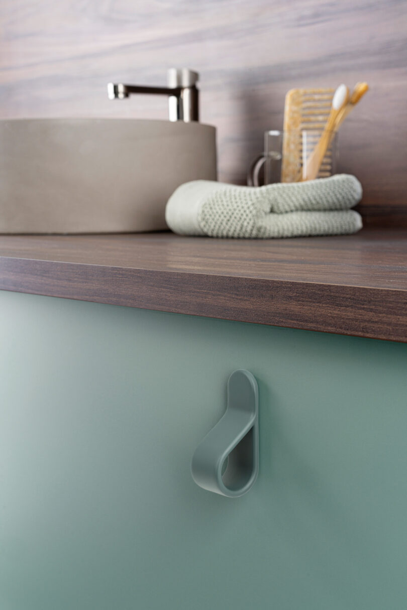 A bathroom counter with a modern faucet, toothbrush holder with brushes, folded towel, and a sleek cabinet door handle below