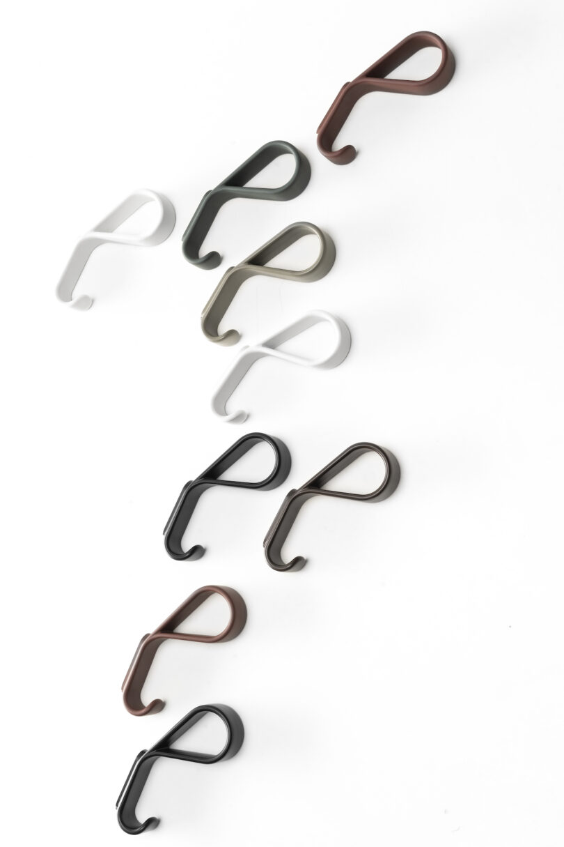 An arrangement of various colored wall hooks on a white background. The hooks are in shades of black, brown, green, and white