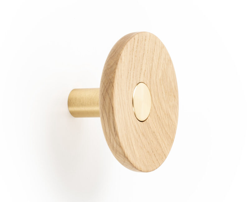 A circular wooden wall hook with a central brass accent mounted on a wall, featuring a brass cylindrical peg