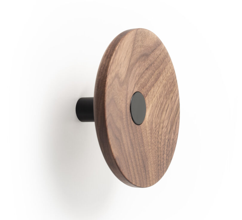 A round, wooden wall hook with a black center and mounting rod, attached to a white wall